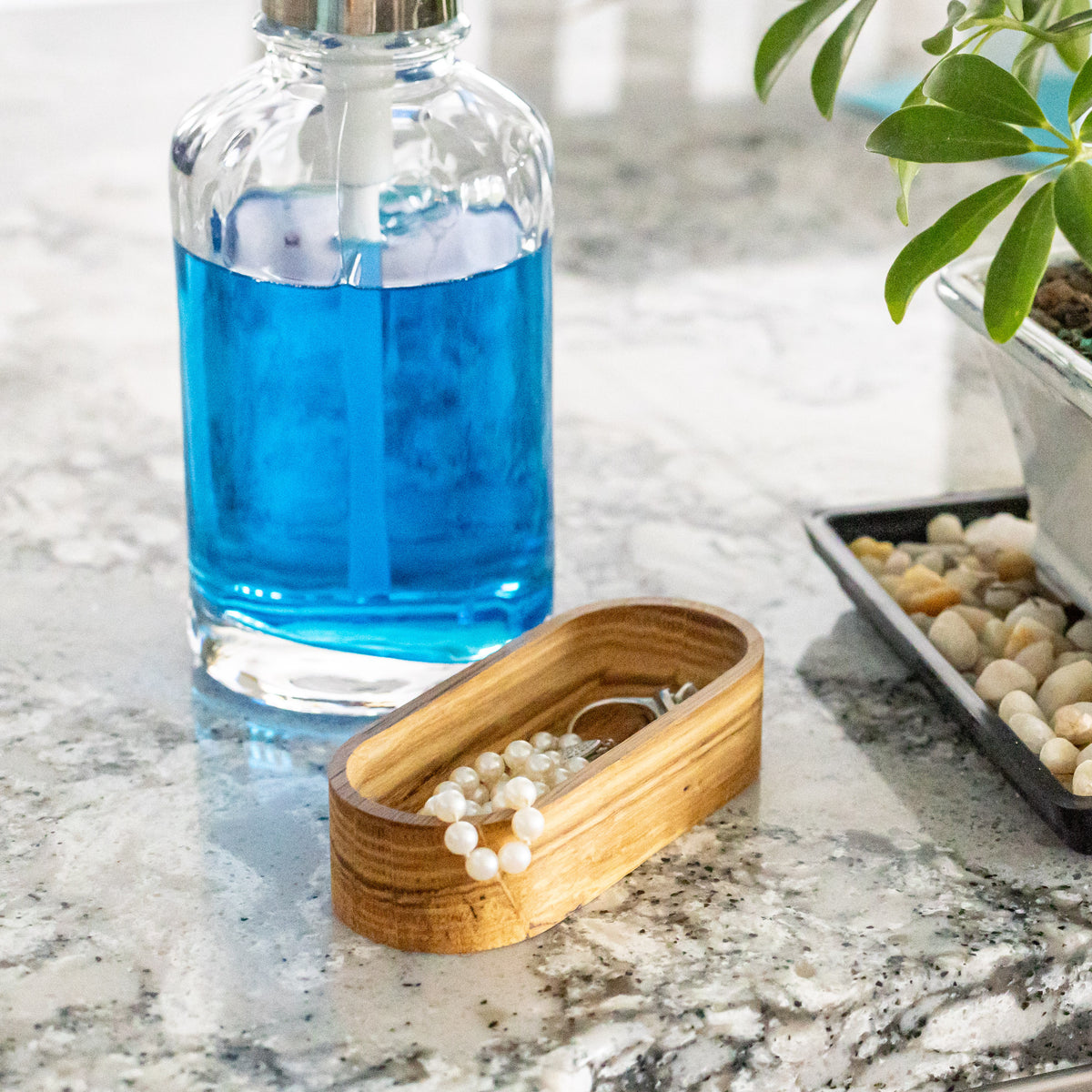 Solid oak oval jewelry dish in use on a bathroom counter with a pearl necklace inside