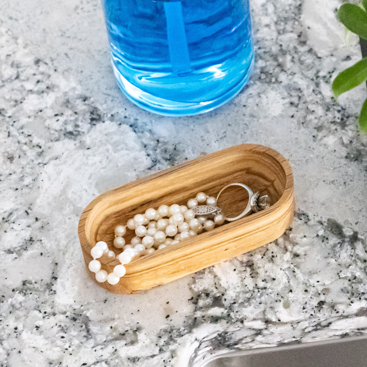 Close-up of a pearl necklace and ring inside a solid oak 4 x 2 inch oval dish